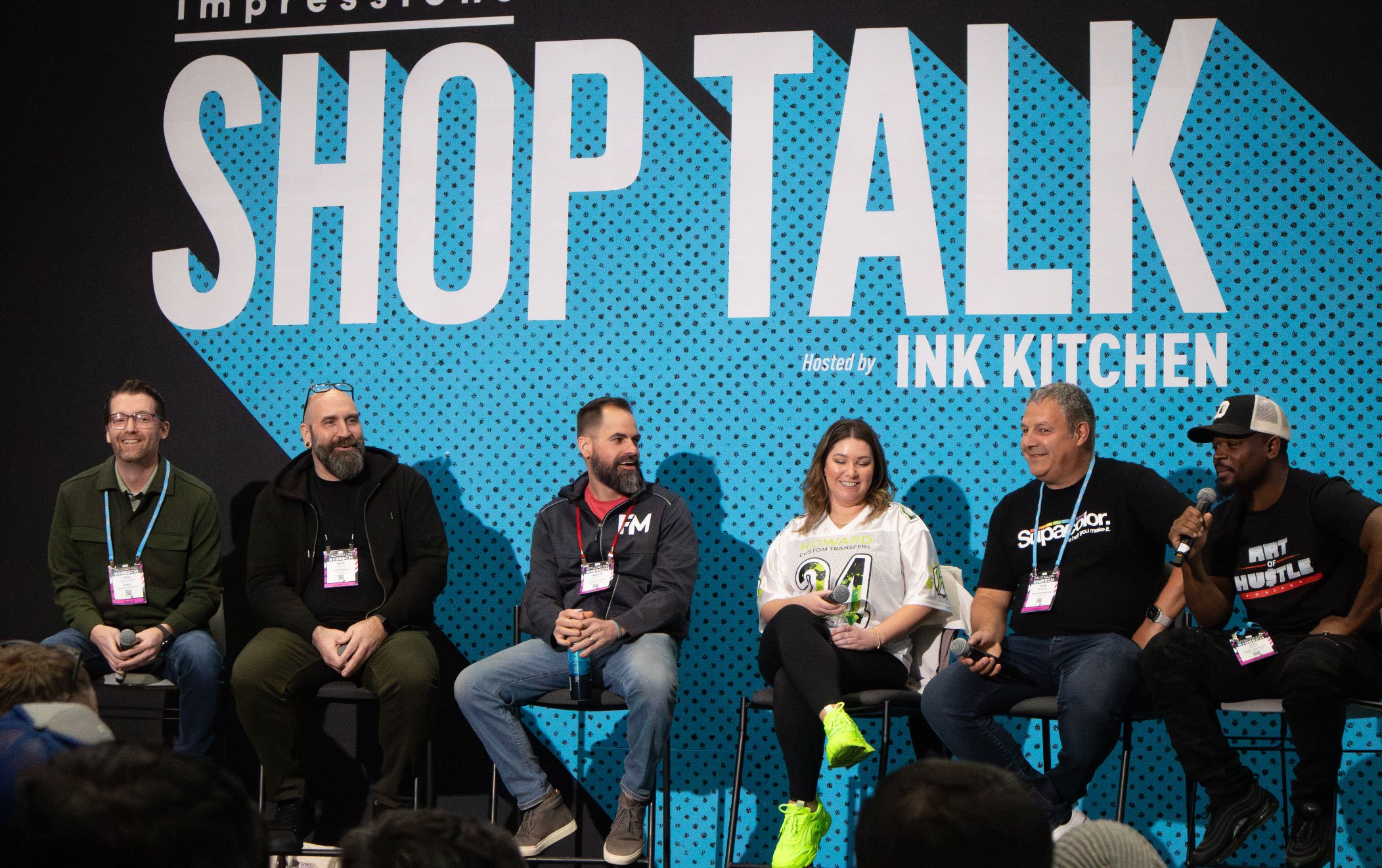  group of people sitting in a row on stage with a "SHOP TALK" sign behind them