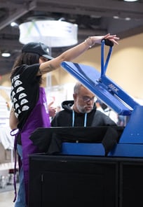 A woman speaking to a man while using a blue heat press to demo products.