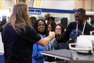 Rick from 613 Originals fist-bumping an excited customer at a trade show while other attendees watch.