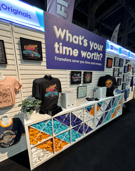 The 613 Originals trade show booth display, featuring a modular shelf with rolled up tshirts in a colorful chevron pattern, hanging garments with applied heat transfers, etc.